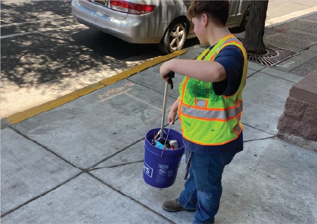 person in high-visibility safety vest using tool to pickup litter