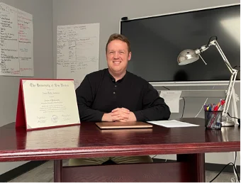 Dr. Anderson smiling at his desk with his doctorate degree on display